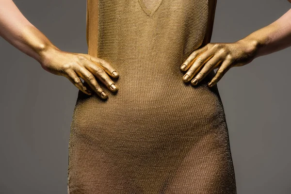 Vista recortada de mujer en vestido dorado y pintura sobre piel posando aislada sobre gris - foto de stock