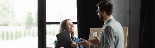 Усміхнена жінка тримає резюме, поки бізнесмен розмовляє під час співбесіди в офісі, банер — стокове фото