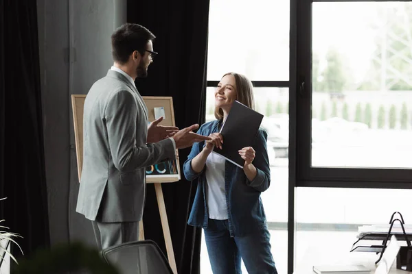Бизнесмен в костюме указывает рукой на жизнерадостную женщину с резюме в офисе — стоковое фото