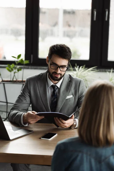 Uomo d'affari in giacca e cravatta che tiene il curriculum vicino alla donna sfocata durante il colloquio di lavoro in ufficio — Foto stock