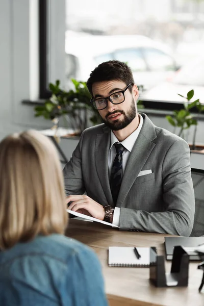 Businessman in formal wear holding resume and talking to blurred woman on job interview — Stock Photo