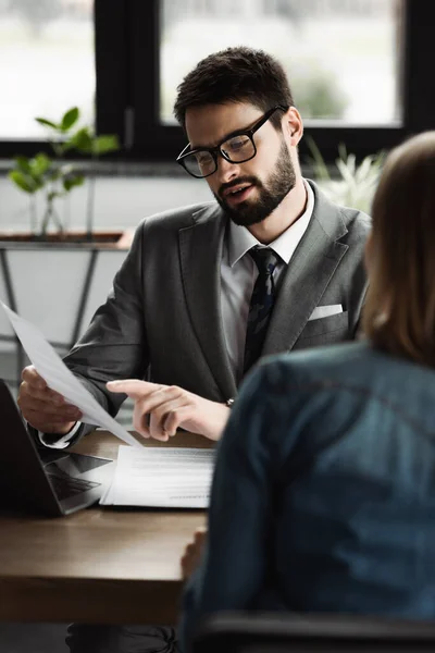 Businessman pointing at resume while talking to blurred candidate on job interview — Stock Photo