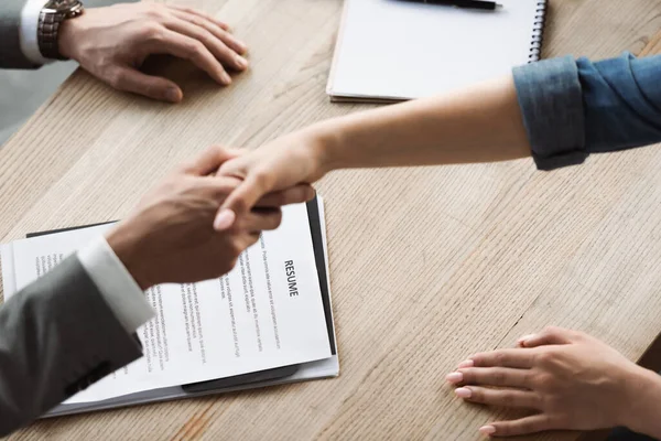 Cropped view of resume near blurred businessman and woman shaking hands during job interview — Stock Photo