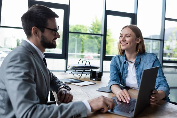 Усміхнена жінка дивиться на бізнесмена біля ноутбука під час співбесіди на роботі в офісі — стокове фото