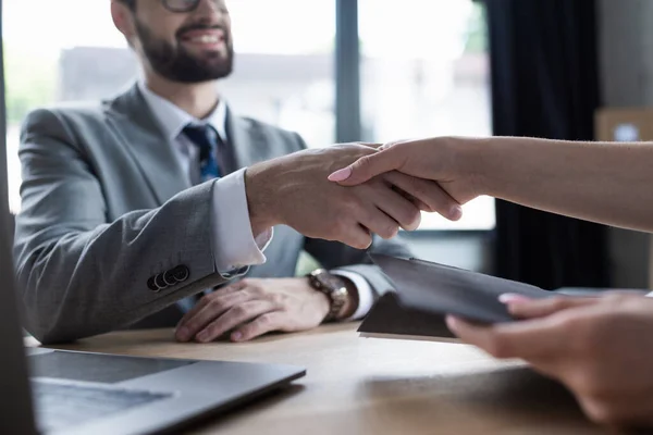 Cropped view of job seeker holding resume and shaking hand of businessman in office — Stock Photo