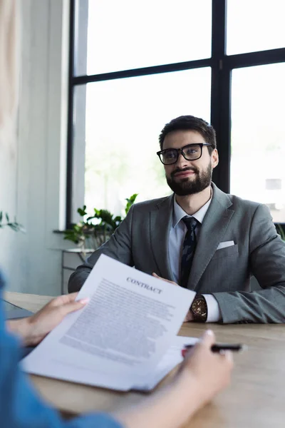 Усміхнений бізнесмен дивиться на розмитого шукача роботи з контрактом в офісі — стокове фото