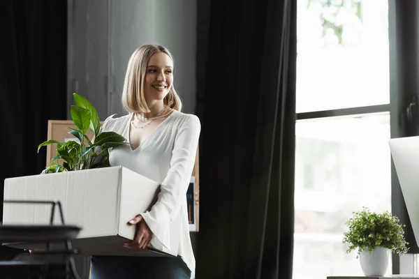 Happy intern holding carton box and looking away in office — Stock Photo