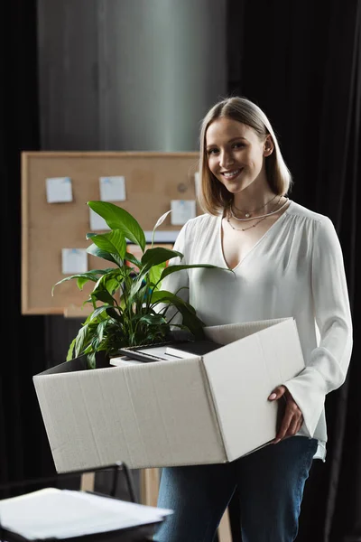 Positive new worker holding carton box with stuff in office — Stock Photo
