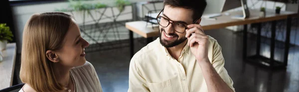 Gestionnaire souriant touchant des lunettes tout en parlant à un stagiaire au bureau, bannière — Photo de stock