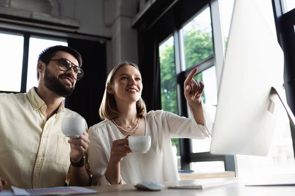 Manager and intern with coffee looking at computer monitor in office — Stock Photo