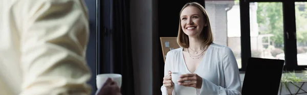 Усміхнений інтерн з чашкою кави дивиться на бізнесмена в офісі, банер — стокове фото