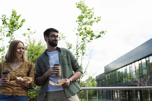 Surprised business people in casual clothes holding coffee to go and sandwiches on urban street — Stock Photo