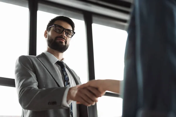 Low angle view of businessman in suit shaking hand of job seeker in office — Stock Photo