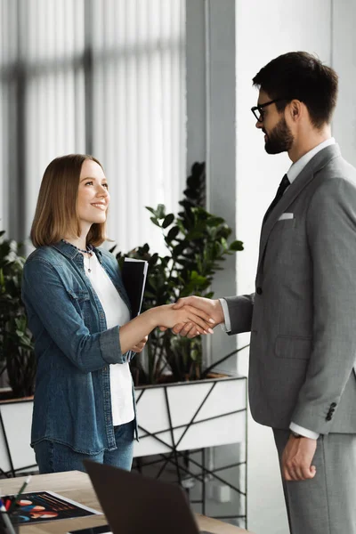 Smiling job seeker holding resume and shaking hand of businessman in office — Stock Photo