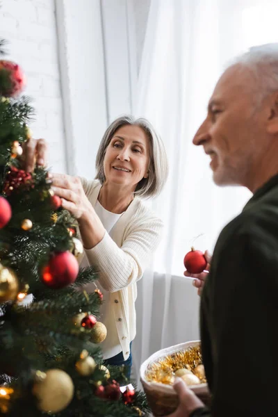 Cheerful middle aged couple decorating christmas tree with baubles — Stock Photo
