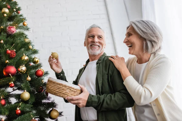 Позитивная женщина средних лет обнимает мужа украшая елку — стоковое фото