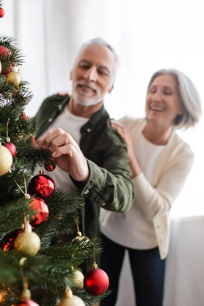 Joyful middle aged woman hugging blurred husband decorating christmas tree — Stock Photo