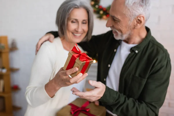Счастливая женщина средних лет, держащая Рождество подарок рядом веселый муж — стоковое фото