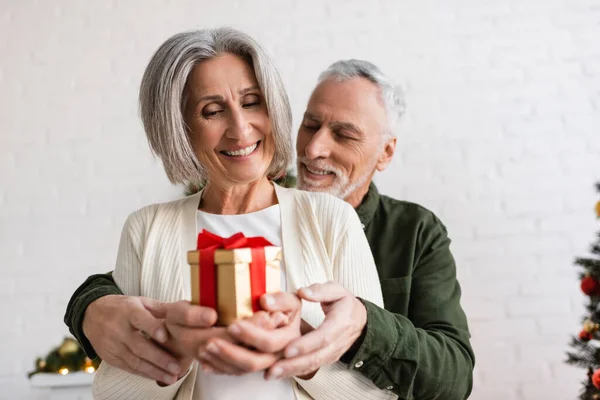Cheerful mature man and happy woman holding christmas present in hands — Stock Photo