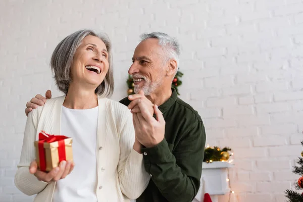Веселий зрілий чоловік тримає руку щасливої дружини з різдвяним подарунком — стокове фото