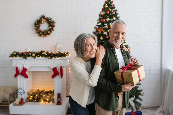 Felice donna di mezza età abbracciando marito barbuto con regalo di Natale — Foto stock