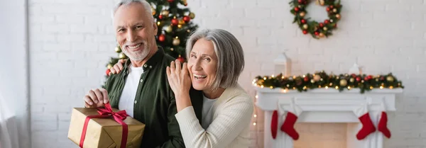 Heureuse femme d'âge moyen étreignant mari barbu avec cadeau de Noël, bannière — Photo de stock