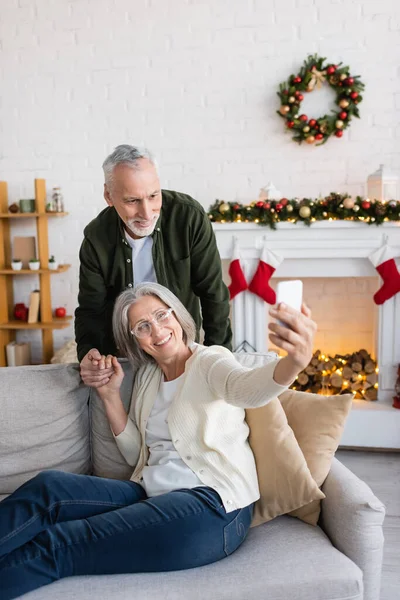 Happy mature woman in glasses taking selfie with husband during christmas — Stock Photo