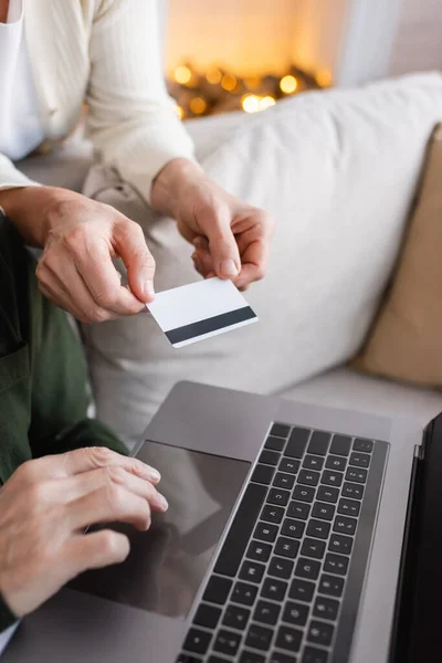 Corte vista de homem maduro usando laptop perto da esposa com cartão de crédito durante feriados de Natal — Fotografia de Stock