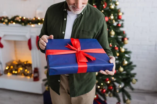 Cropped view of happy and bearded middle aged man holding wrapped present near christmas tree — Stock Photo