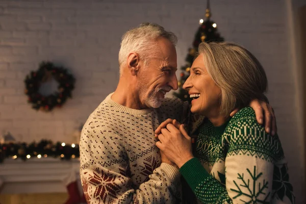 Fröhlich reifer Mann im festlichen Pullover umarmt freudige Frau an Heiligabend — Stockfoto