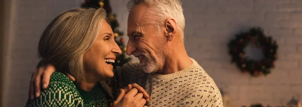 Fröhlicher reifer Mann im festlichen Pullover umarmt freudige Frau am Heiligabend, Banner — Stockfoto