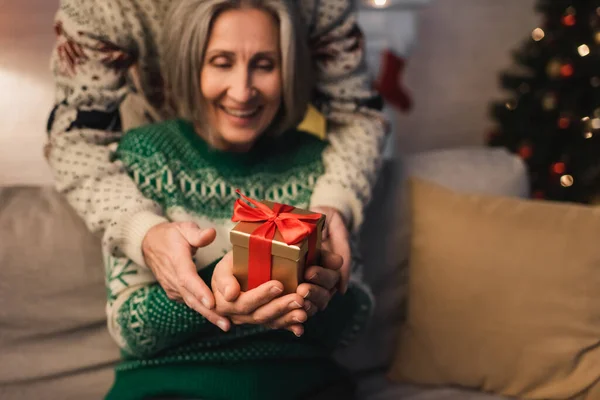 Cheerful middle aged couple in festive sweaters holding christmas present in hands — Stock Photo