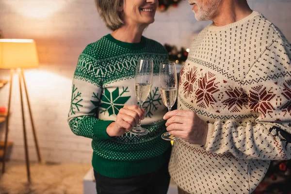 Abgeschnittene Ansicht eines glücklichen Paares mittleren Alters in festlichen Pullovern, die Champagnergläser klirren — Stockfoto