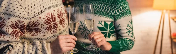 Обрезанный вид пары средних лет в праздничных свитерах, звон бокалов шампанского, баннер — стоковое фото