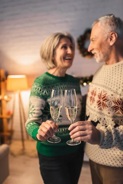 Casal de meia idade desfocado e feliz em camisolas festivas copos de champanhe — Fotografia de Stock