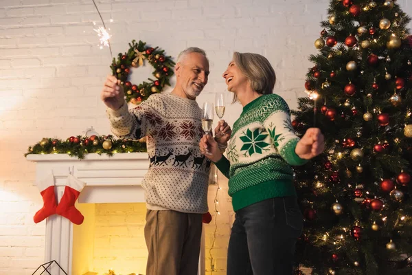 Позитивна зріла пара в светрах тримає келихи шампанського і блискітки на Різдво — стокове фото