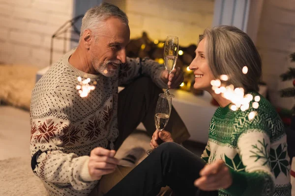 Щаслива пара середнього віку тримає келихи шампанського і блискучі блискавки на Різдво — стокове фото