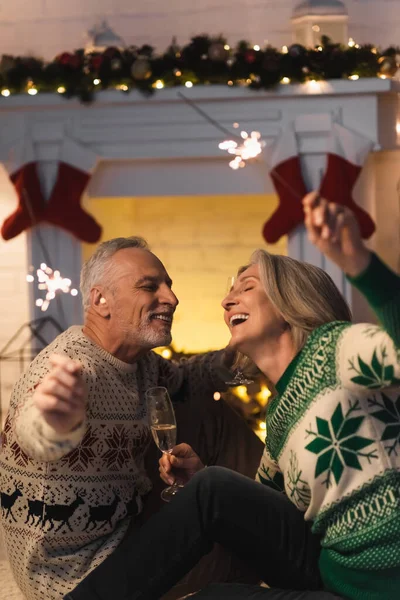 Alegre casal maduro segurando copo de champanhe e brilhos brilhantes na véspera de Natal — Fotografia de Stock