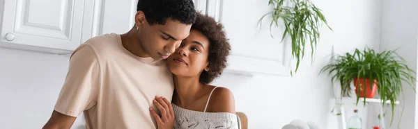 Pleased and sexy african american woman hugging young boyfriend in kitchen, banner — Stock Photo