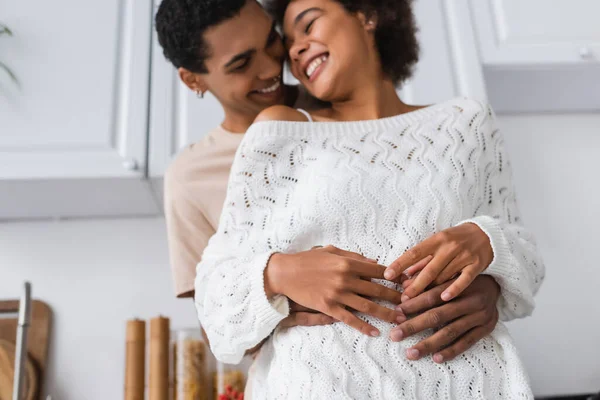 Baixo ângulo vista de homem borrado abraçando rindo afro-americana namorada na cozinha — Fotografia de Stock