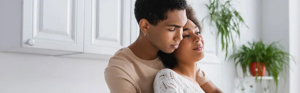 Young african american woman smiling and looking away near young man in kitchen, banner — Stock Photo