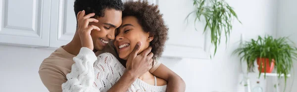 Jovem casal afro-americano sorrindo e abraçando com os olhos fechados na cozinha, bandeira — Fotografia de Stock