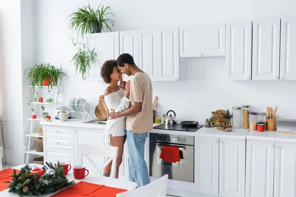 Jovem e sexy casal afro-americano abraçando na cozinha espaçosa com mobiliário branco — Fotografia de Stock