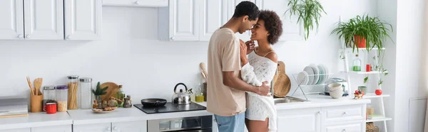 Alegre casal afro-americano abraçando enquanto de pé cara a cara na cozinha moderna, banner — Fotografia de Stock