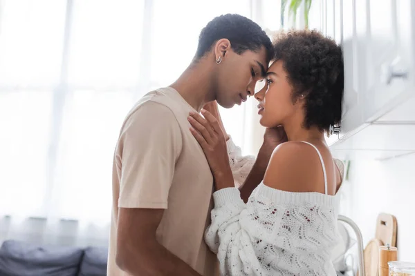 Side view of african american man in t-shirt and sexy woman in knitted sweater standing face to face in kitchen — Stock Photo