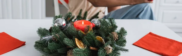 Spruce wreath decorated with candle and christmas balls near cropped african american man, banner — Stock Photo