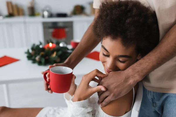 Afrikanisch-amerikanischer Mann mit roter Tasse berührt sinnliche Freundin in Küche — Stockfoto