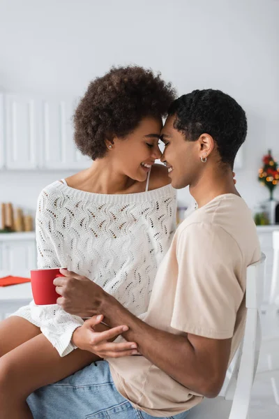 Seductora mujer afroamericana en suéter blanco sentada cara a cara con su novio en la cocina - foto de stock