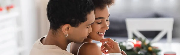 Jeune homme afro-américain toucher menton de petite amie heureuse dans la cuisine floue, bannière — Photo de stock