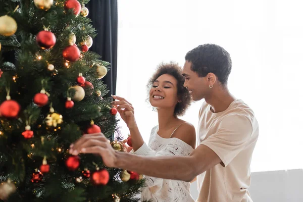Молодая и сексуальная африканская пара, украшающая рождественскую елку дома — стоковое фото